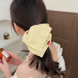 Detail of yellow striped bow hair scrunchie with red cherry embroidery worn by a model