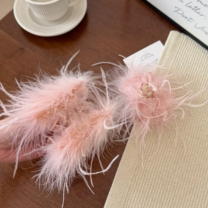 Detailed close-up of soft pink ostrich feather hair claw clip on a cozy wooden table