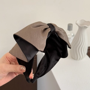 Détail d'un large serre-tête à nœud en tissu texturé marron et base élégante en satin noir