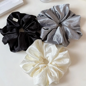 Three-piece set of satin camellia flower scrunchies in black, silver, and cream colors