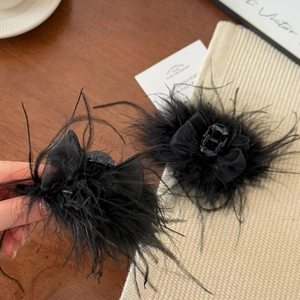Close-up of black ostrich feather hair claw clip with fluffy texture on a wooden desk