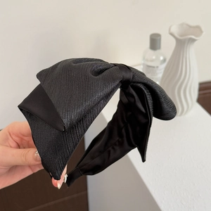 Détail d'un serre-tête à gros nœud noir avec tissu scintillant et design volumineux