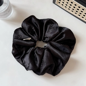 Detail of black satin hair scrunchie with camellia embroidery and minimalist label