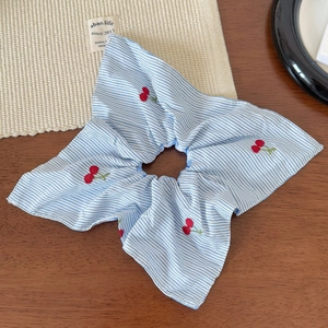 Detailed shot of blue and white striped scrunchie with red cherry embroidery texture
