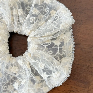 White lace scrunchie with floral embroidery and bead trim edges on dark wood