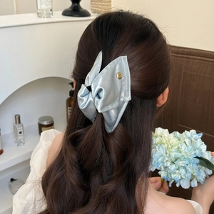Back view of a light blue satin bow hair clip on a woman's long wavy dark brown hair