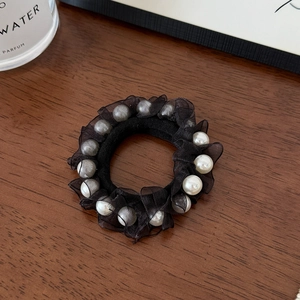 Close-up of black mesh hair scrunchie with elegant faux pearl accents on wood surface