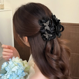 Elegant black ribbon bow hair claw clip with rhinestones shown on brown wavy hair