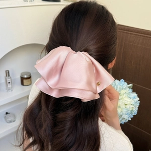 Elegant large light pink satin bow hair clip styled on long wavy hair in home setting