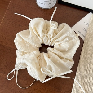 Gros plan détaillé d'un chouchou beige avec pompons blancs et nœud en ruban élégant