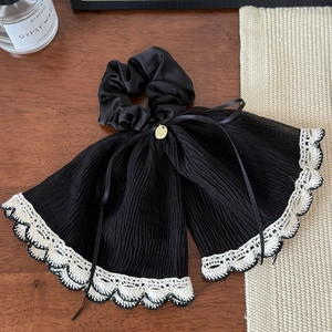 Détail d'un chouchou plissé noir avec dentelle blanche et petit charm doré