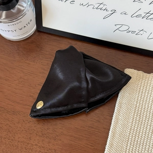 Detailed texture of black satin fabric hair claw with a small gold believe metal badge