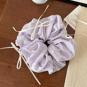 Détail du chouchou lavande à pois avec des nœuds blancs sur une table en bois
