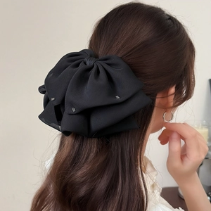 Detail of a large black multi-layer bow hair claw with rhinestones on long wavy hair