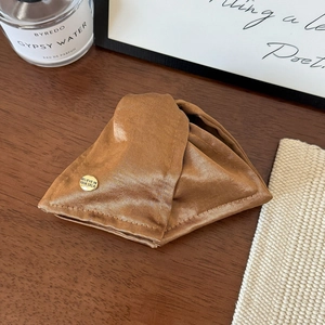 Detail of a brown satin hair claw clip with a luxury gold logo charm on a wooden desk