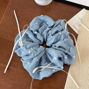 Détail d'un chouchou bleu clair en velours à pois avec des nœuds en ruban blanc