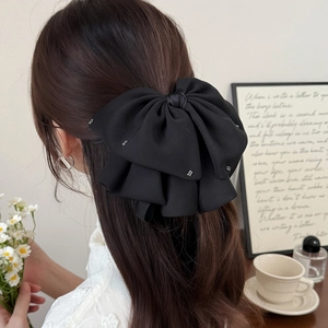 Elegant black layered bow hair clip with rhinestones worn on a half-up hairstyle