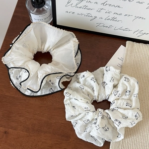Dettaglio di scrunchies bianco crema con stampe di gatti e bordi neri a contrasto su legno
