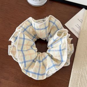 Detail of a plaid scrunchie with lace edges on a wooden background with accessories