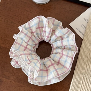 Detail of pink and blue plaid scrunchie with white lace trim on wooden background