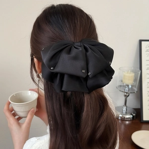 Detail view of large black satin bow hair clip with silver rhinestones on long brown hair