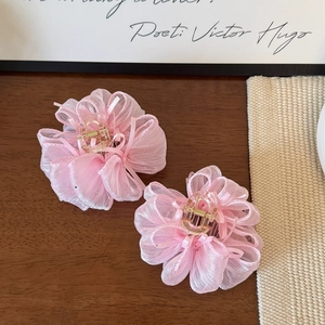 Dettaglio di due mollette per capelli a fiori in organza rosa su una scrivania in legno