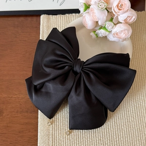 Dettaglio di un grande fiocco per capelli in raso nero con piccoli ciondoli dorati ed eleganti