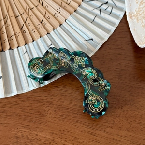 Détail d'une pince à cheveux marbrée vert foncé avec des motifs de nuages dorés