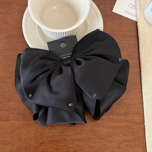 Close-up of a black silk bow hair claw clip with square rhinestones on a wooden desk