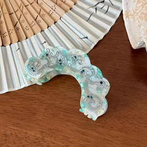 Détail d'une pince à cheveux en acétate marbré vert avec dragon argenté et strass bleus