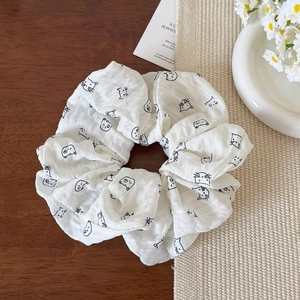 Dettaglio di uno scrunchie bianco crema con stampa di gatti su un tavolo in legno