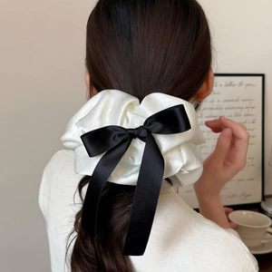 Détail d'un chouchou en satin blanc plissé avec un grand nœud noir sur les cheveux du mannequin