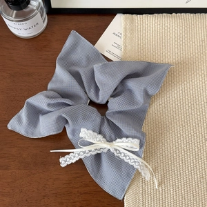 Detail of blue and white checkered scrunchie with lace bow on a rustic wooden desk