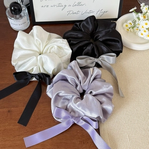 Trois chouchous en satin avec nœuds en blanc, noir et violet sur un bureau en bois chic