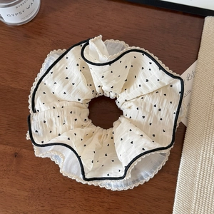Close-up of beige chiffon hair scrunchie with black heart print and lace trim edges