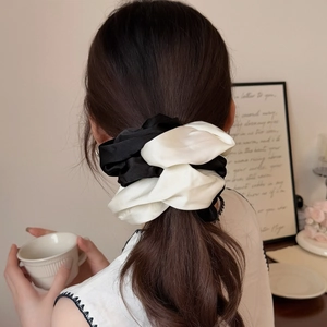 Elegant black and white contrast satin scrunchie shown on a ponytail in a cozy setting