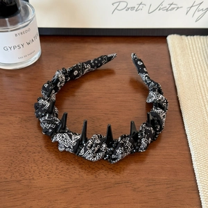 Close-up of black paisley headband with gothic spikes and beads on wooden surface