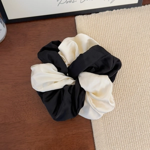 Detailed view of black and white contrast satin scrunchie on a dark wooden table