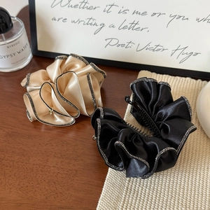Vue détaillée de pinces banane en satin plissé or et noir avec bords en strass