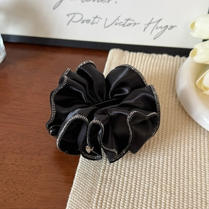 Détail d'une pince à cheveux en satin plissé noir avec bordure en strass argentés