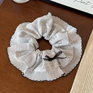 Détail du chouchou à carreaux gris et blanc avec bords ondulés noirs et un nœud