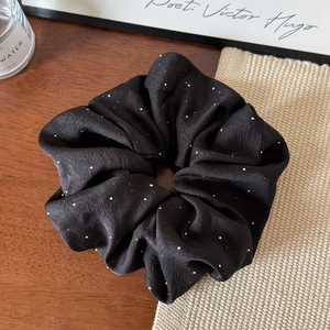 Close-up of black satin scrunchie with white polka dots and elegant fabric pleats