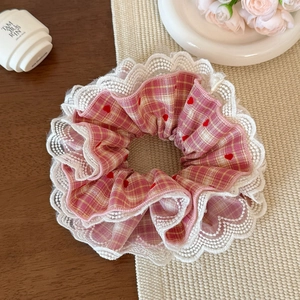 Pink checkered hair scrunchie with red hearts and white lace edge detail shown on table