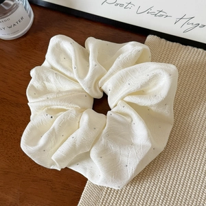 Close-up of cream pleated fabric scrunchie with sparkling rhinestones on wooden table