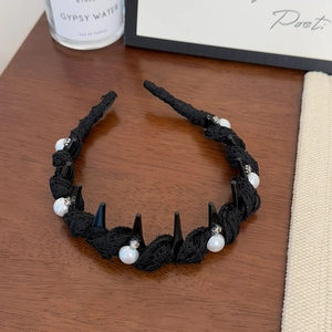 Detail of black lace headband featuring pearls, rhinestones, and studs on a wood surface