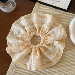 Vue détaillée du chouchou vichy jaune avec bordure en dentelle blanche sur une table