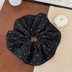 Detail eines schwarzen gepunkteten Scrunchies auf Holztisch mit elegantem Zubehör