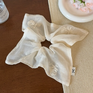 Close-up of beige scrunchie with rose embroidery and brand logo on wooden table