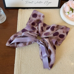 Detail of purple leopard print scrunchie with silk ribbons on a decorative wooden table