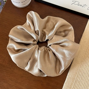 Detail eines eleganten Satin-Haargummis in Champagnergold mit seidiger Textur auf Holz